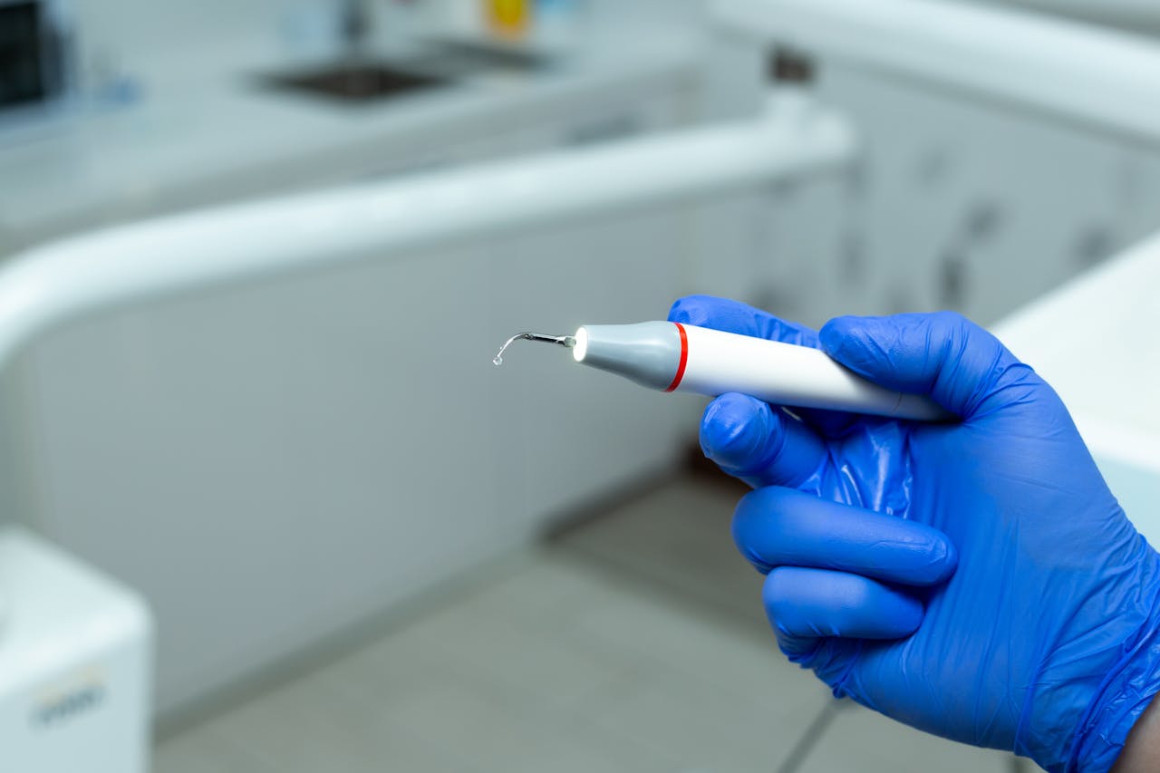 A dentist holds a dental scaler tool in a clinic, wearing blue gloves.